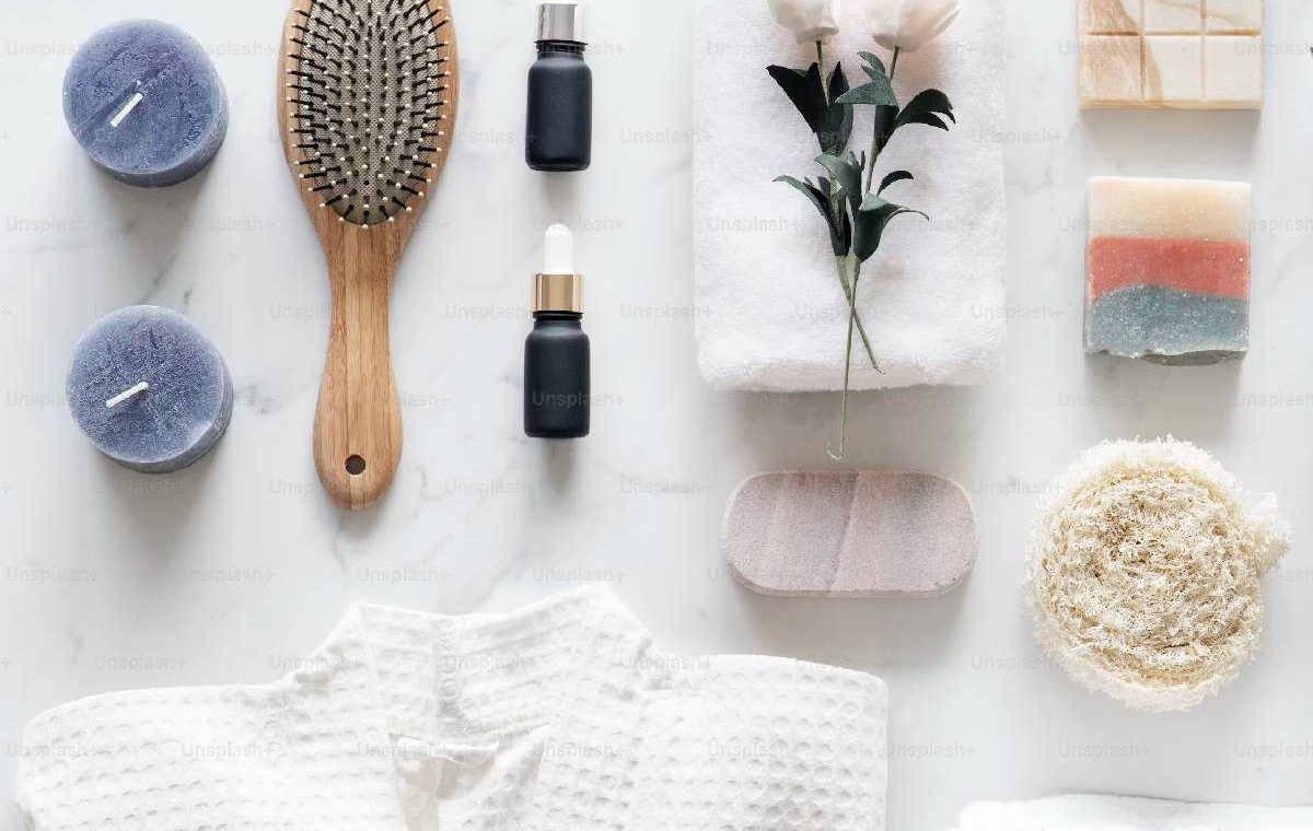 Candles, a hairbrush, soaps and towels laid out on a white table